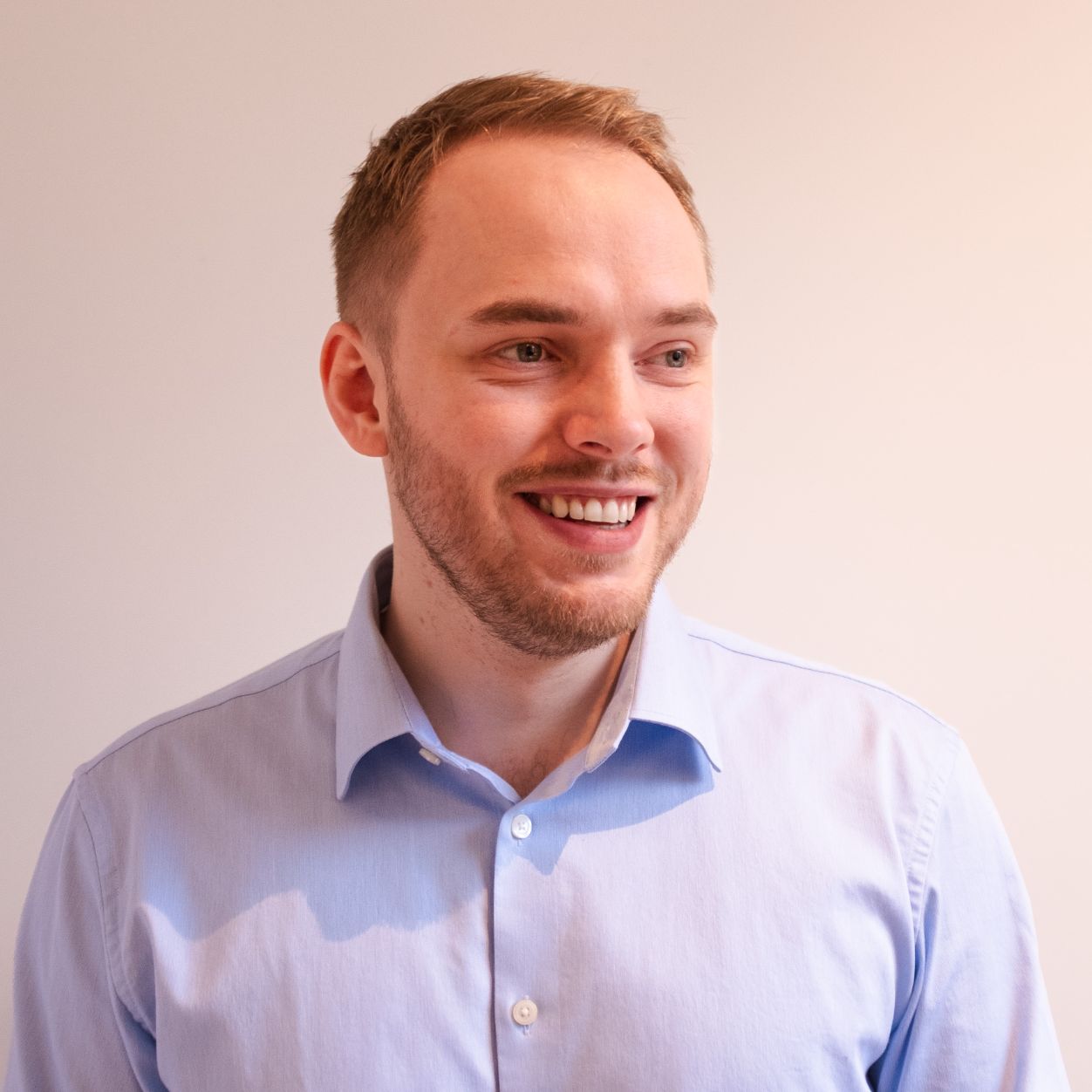 Erlend Aasen Portrett av smilende mann med lyst hår og blå øyne, ikledd lyseblå skjorte